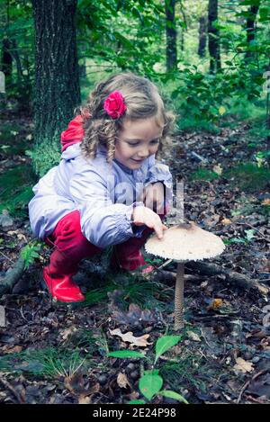 Lächelndes Mädchen berührt einen Pilz wächst im Wald, Polen Stockfoto