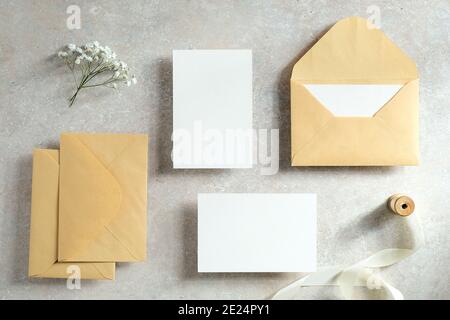 Hochzeitseinladungen und Schreibwaren Draufsicht. Leere Papierkarten Mockups, Kraftpapier Umschläge, Band, Blumen auf Stein-Tisch. Vintage-Style. Flach liegend. Stockfoto