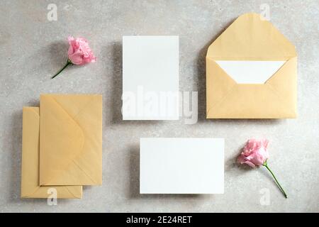 Hochzeitseinladungskarten und Schreibwaren Draufsicht. Flach legen unbeschriftete Papierkarte, Kraftpapier Umschläge, Blumen auf Stein-Tisch. Vintage-Style. Stockfoto