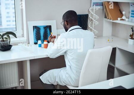 Medizinischer Mann, der sich über ein Testglas des Impfstoffes lehnt Stockfoto
