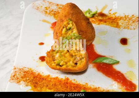Reis arancini, traditionelle sizilianische Fleischbällchen, Italien, mit Reis, Fleisch, Erbsen und Sauce, paniert und gebraten. Ein Ganzes und ein in die Hälfte geschnitten Stockfoto
