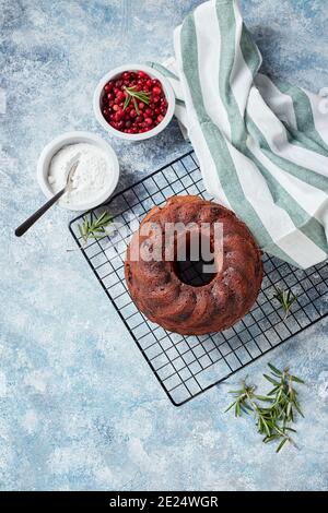 Schokoladenkuchen auf einem Metalldrahtgestell, Puderzucker und Preiselbeeren in Schalen, für die Dekoration vorbereitet Stockfoto