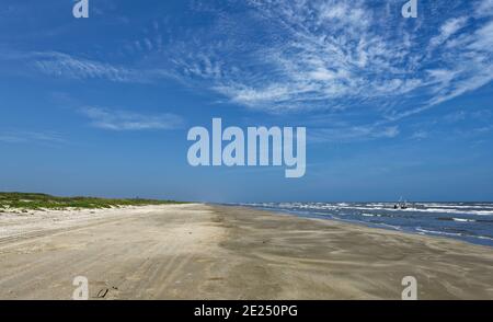 Blick auf den menschenleeren Strand auf Padre Island in der Nähe des Besucherzentrums an einem lebhaften Tag im Juni, mit den niedrigen Sanddünen bedeckt mit Gras und Railro Stockfoto