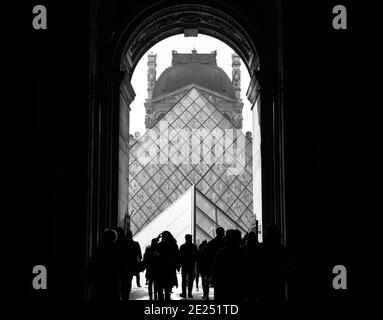 Menschen und Kunst. Silhouetten von Touristen, die durch den Durchgang zur Pyramide des Louvre gehen. Schwarz weiß historische konzeptionelle Foto Stockfoto