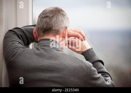 Trauriger reifer Mann, der sich an einem Fenster mit Regentropfen lehnt - Konzentrieren Sie sich auf die Hände und das Fenster Stockfoto