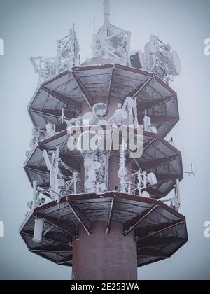 Ein gefrorener stillgedeckter Funkturm mit Neuschnee. Die gefrorene Antenne und Antennen sind mit gefrorenem Neuschnee bedeckt. Stockfoto