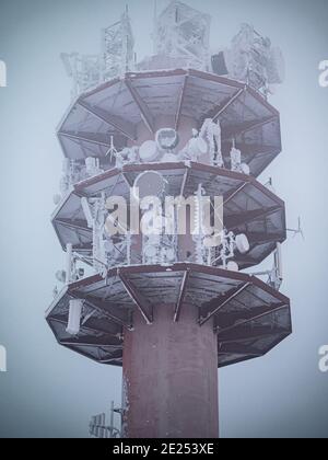 Ein gefrorener stillgedeckter Funkturm mit Neuschnee. Die gefrorene Antenne und Antennen sind mit gefrorenem Neuschnee bedeckt. Stockfoto