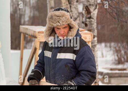 Porträt eines Mannes in einem Hut mit hellem Fell Mit einer blauen Winterjacke am Arbeitsplatz Stockfoto