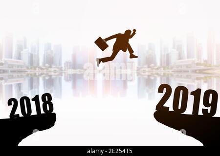 Silhouette des jungen Geschäftsmann Springen zwischen 2018 und 2019 Jahren mit schönen Wolkenkratzern Hintergrund, Konzepte des Nachrichtenjahres und Business targ Stockfoto