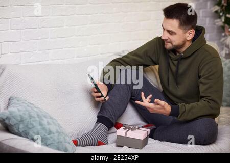Schöner junger Mann mit Smartphone für Online-Dating mit seiner Freundin, während ein Geschenk zu Hause halten. Stockfoto