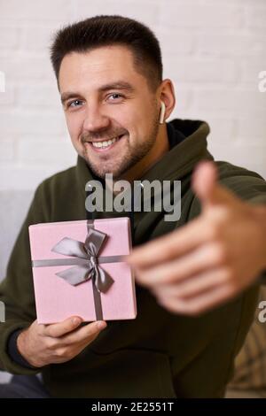 Portrait von lächelnd schönen jungen Mann in Kopfhörer mit einem Geschenk-Box. Der Kerl ist im Gespräch mit seiner Freundin auf der Online-Verbindung Stockfoto