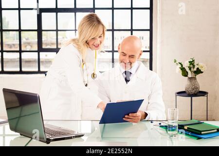 Aufnahme eines männlichen Arztes, der am Schreibtisch sitzt, während eine Ärztin neben ihm steht und sich berät. Gruppe von medizinischen Team arbeitet zusammen in den Ärzten von Stockfoto