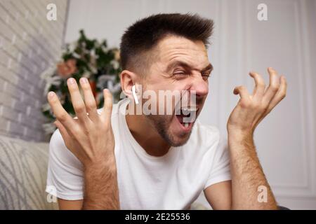 Wütend schreienden jungen Mann in Ohrhörern spricht mit jemandem auf Videoanruf. Stockfoto