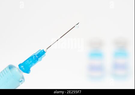 Medizinisches Konzept - Nahaufnahme der Spritze mit Nadel mit blauer Flüssigkeit. Verschwommener Hintergrund mit Impffläschchen. Speicherplatz kopieren. Stockfoto