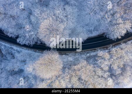 Csesznek, Ungarn - Luftaufnahme von oben nach unten von Winterwald gekreuzt von Asphaltstraße. Verschneite Landschaft Hintergrund. Stockfoto