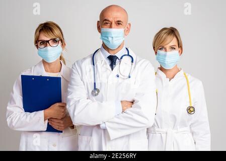 Aufnahme von weiblichen und männlichen Ärzten, die vor isoliertem Hintergrund zusammenstehen. Medizinisches Team. Ärzte tragen Gesichtsmasken zur Prävention. Stockfoto