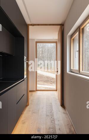 Modernes Interieur mit weißen Wänden und Parkettböden. Stilvolle schwarze Küche mit großen Fenstern zur Natur. Niemand drinnen Stockfoto