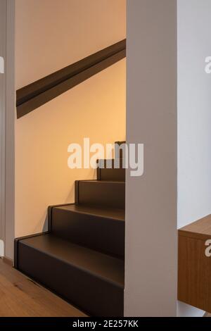 Moderne Inneneinrichtung mit weißen Wänden und Parkett auf dem Boden. Detail der schwarzen Stufen einer Treppe. Niemand drinnen Stockfoto