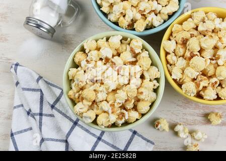 High-Angle-Schuss von drei verschiedenen farbigen Schüsseln von frischem Popcorn mit Tüchern und Salz Shaker mit Salz verschüttet. Stockfoto