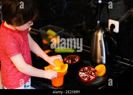 Kleiner Junge, der frischen Orangensaft zubereitet und Orangen in der Küche quetscht. Stockfoto