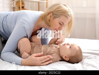 Liebevolle blonde Mutter streichelt ihren kleinen Jungen auf dem Bett Stockfoto