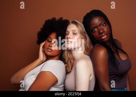 Junge hübsche kaukasische, afro, skandinavische Frau posiert fröhlich zusammen auf braunem Hintergrund, Lifestyle diverse Nationalität Menschen Konzept Stockfoto