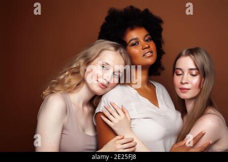 Junge hübsche kaukasische, afro, skandinavische Frau posiert fröhlich zusammen auf braunem Hintergrund, Lifestyle diverse Nationalität Menschen Konzept Stockfoto