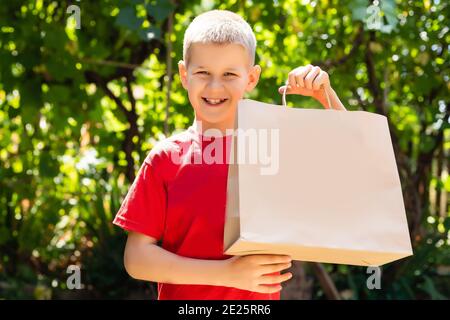 Glücklicher Junge mit Einkaufstaschen. Sommerverkauf, schwarzer freitag. Cyber montag. Große Verkäufe für Kinder. Handwerk Pakete in der Hand. Viele Einkäufe und Geschenke. Stockfoto