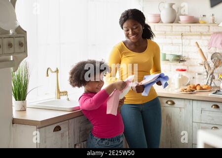 Cute African American Girl Hilft Mutter Mit Haushalt, Abwischen Geschirr In Der Küche Stockfoto