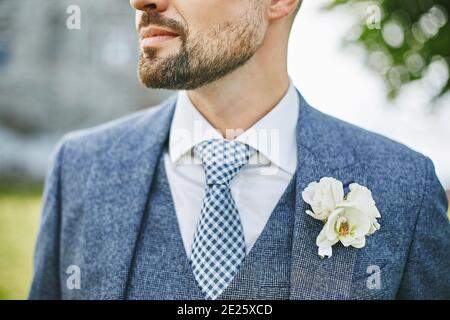 Ein Porträt eines unerkennbaren, hübschen Mannes mit Bart und Schnurrbart in Krawatte und einem eleganten dreiteiligen Anzug mit Boutonniere. Stilvoller Bräutigam Stockfoto