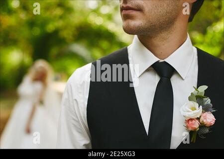 Beschnittenes Porträt eines unerkennbaren schönen Mannes in schwarzer Krawatte und eleganter Weste mit Boutonniere. Stilvoller Bräutigam wartet auf die Braut Stockfoto