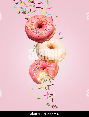 Zwei Donuts Donuts fallen auf einen rosa Hintergrund mit Streuseln hinter ihnen mit Kopieplatz und Platz für Text. Stockfoto