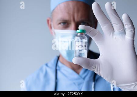 Kaukasischen männlichen Arzt trägt Gesichtsmaske stehen und zeigt Coronavirus Impfstoff Stockfoto