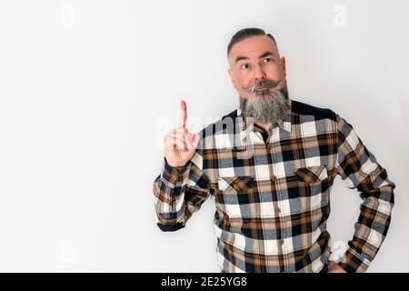 Hipster mit eigenartiger Erscheinung, großem Bart und Schnurrbart und witzigem Ausdruck, der Zeigefinger der Hand mit einer lustigen und originellen Geste hebt Stockfoto