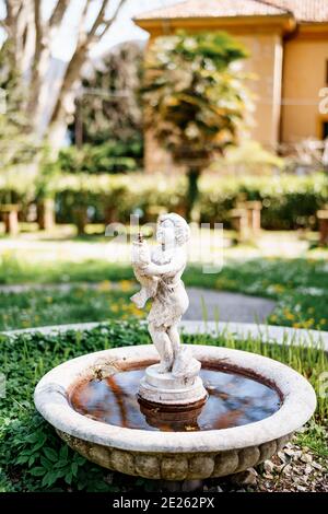 Ein kleiner Gartenbrunnen in Form einer Figur eines Kindes mit einem Fisch in den Händen im Hof. Stockfoto