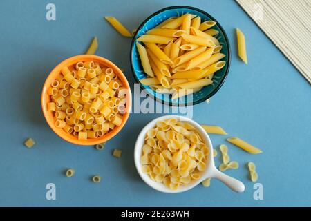 penne, farfalle tonde Schmetterling und Ditalini Art von Pasta auf hellblauem Hintergrund. Pasta in Keramik-Schüssel. Blau orange weiße Schale. Abstrakt, Pasta. t Stockfoto