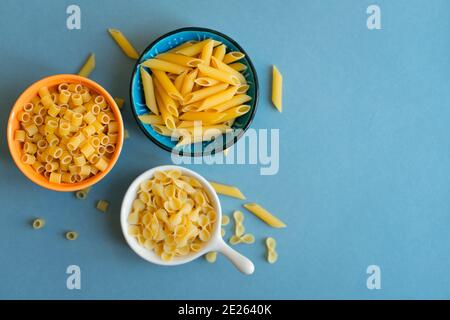 penne, farfalle tonde Schmetterling und Ditalini Art von Pasta auf hellblauem Hintergrund. Pasta in Keramik-Schüssel. Blau orange weiße Schale. Abstrakt, Pasta. t Stockfoto