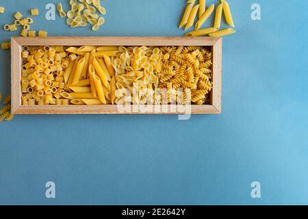 penne, farfalle tonde Schmetterling, Schnecke und Ditalini Art von Pasta auf hellblauem Hintergrund. Pasta in einer Holzkiste Teller. Abstrakt, Pasta. Draufsicht Pho Stockfoto
