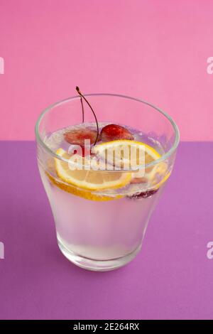 Ein Glas Sekt Cocktail mit Zitrone, Kirsche und Beere in Scheiben geschnitten. Alkoholfreie Getränke, Getränke. Lila strukturierte Hintergrund und rosa Hintergrund. Stockfoto