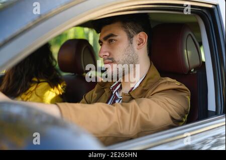 Junger bärtiger hispanischer Mann, der mit seiner Freundin ein Auto fährt Stockfoto