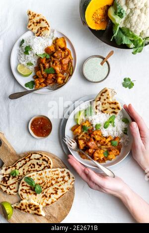 Draufsicht auf ein vegetarisches, veganes indisches Balti-Curry mit Blumenkohl und Kürbis, serviert mit Raita, Naan-Brot und Mango-Chutney und Basmati Stockfoto