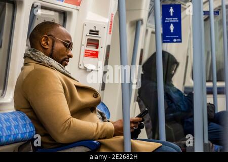 London, Großbritannien. Januar 2021. Ein Mann scheint entspannt zu sein, keine Maske zu tragen, trotz der Schilder über ihm und dem Aussehen anderer maskierter Passagiere - die U-Bahn ist trotz der neuen nationalen Sperre, Aufenthalt zu Hause, Anweisungen immer noch ziemlich voll. Die meisten Reisenden tragen Masken, da sie bereits obligatorisch sind. Kredit: Guy Bell/Alamy Live Nachrichten Stockfoto