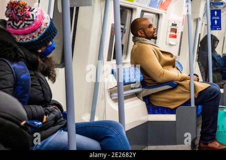 London, Großbritannien. Januar 2021. Ein Mann scheint entspannt zu sein, keine Maske zu tragen, trotz der Schilder über ihm und dem Aussehen anderer maskierter Passagiere - die U-Bahn ist trotz der neuen nationalen Sperre, Aufenthalt zu Hause, Anweisungen immer noch ziemlich voll. Die meisten Reisenden tragen Masken, da sie bereits obligatorisch sind. Kredit: Guy Bell/Alamy Live Nachrichten Stockfoto