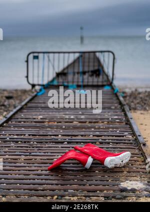 Verlorene Red Wellies am Strand - hinter roten wellington-Stiefeln auf einem Küstensteg am Strand zurückgelassen. Rote Stiefel. Rote Gummistiefel. Stockfoto
