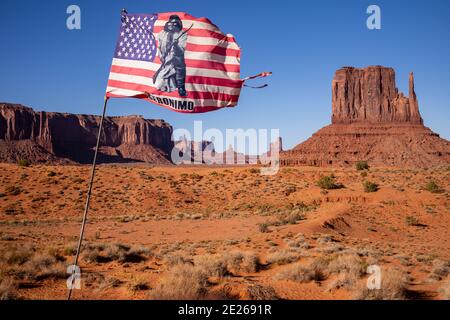 Die US-Flagge mit einem Bild des Apache-Führers Geronimo vor den West Mitten und Sentinel Mesa, Monument Valley Navajo Tribal Park, USA Stockfoto