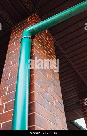 Kunststoff-grünes Entwässerungsrohr an der Wand des Hauses Wasser vom Dach in den Boden ablassen Stockfoto