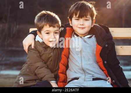 Zwei niedliche Jungen, Brüder, sitzen auf einer Bank, liebevoll miteinander. Stockfoto