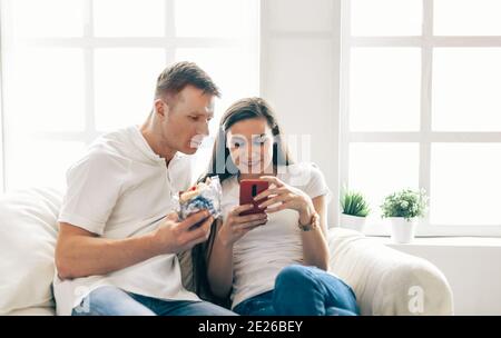 Junges Paar mit Smartphone auf einem bequemen Sofa sitzen. Stockfoto