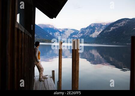 Junge Frau steht am See, umgeben von Bergen bei Sonnenuntergang. Stockfoto