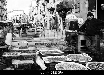 NEAPEL, ITALIEN - 15. DEZEMBER 2019: Straßenmarkt. Senior Mann verkauft Meeresfrüchte - Vielfalt an frischen Muscheln, Krebstiere, etc. Schwarz weiß Foto. Stockfoto